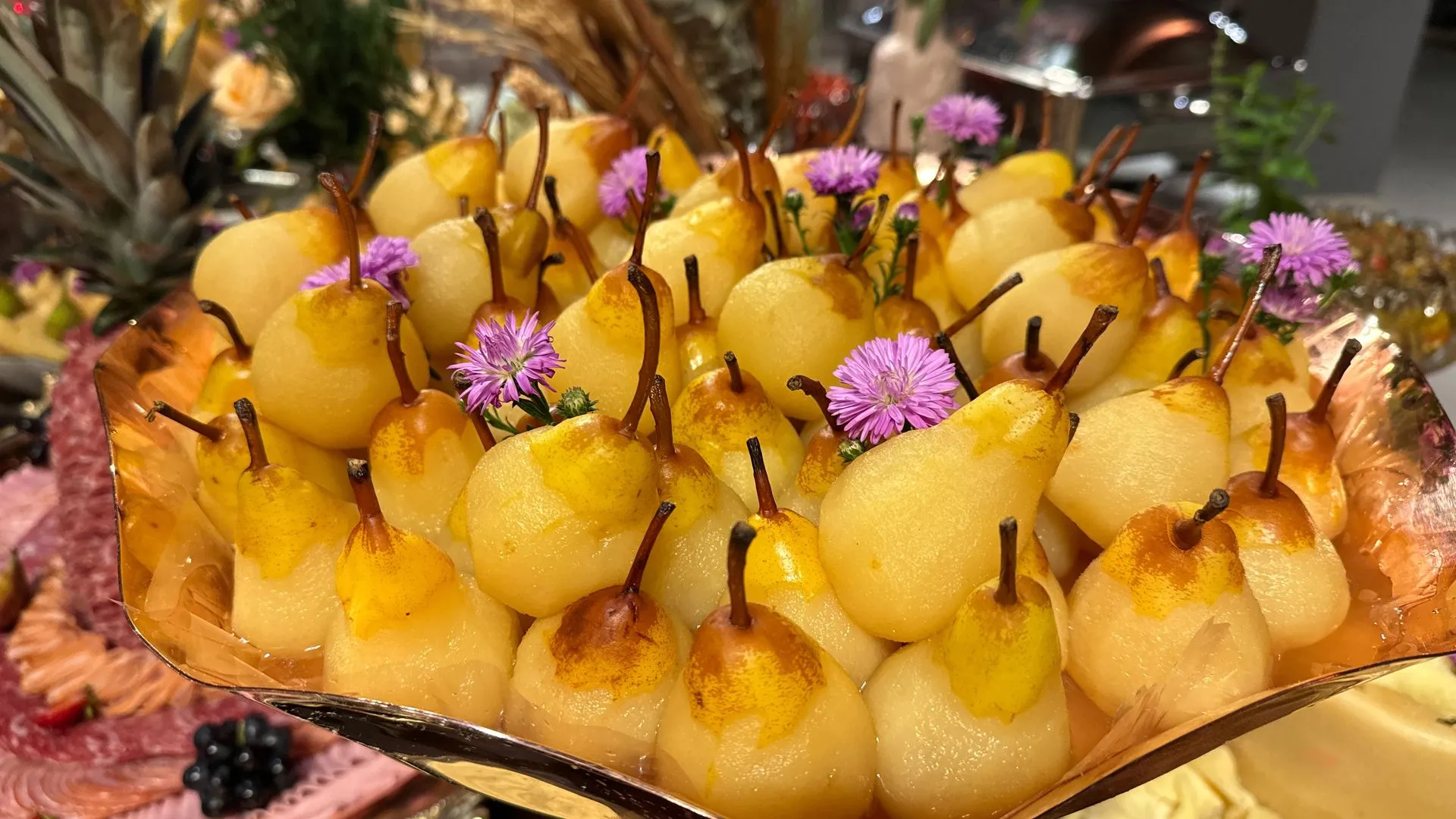 Um prato de peras com flores roxas em cima de uma mesa.