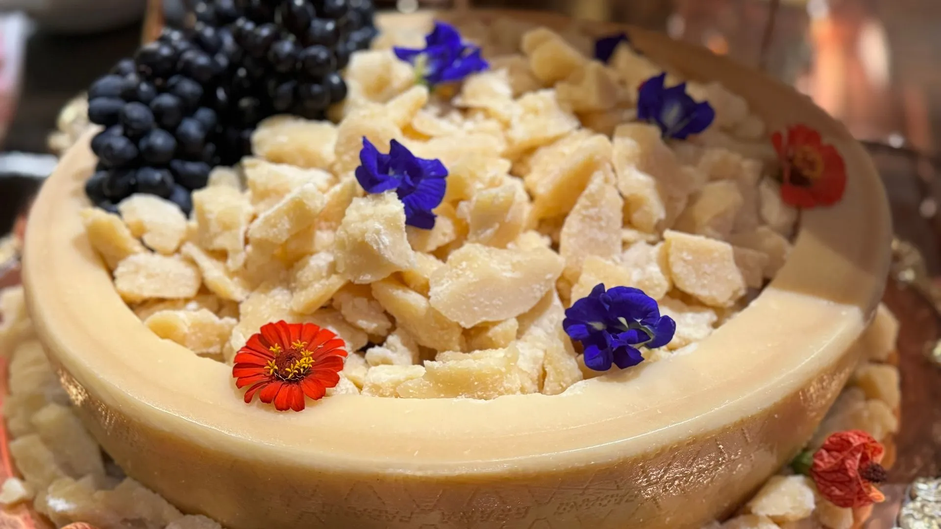 Um pedaço de queijo com flores e mirtilos por cima.