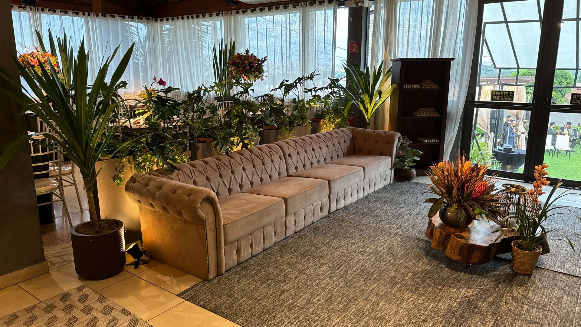 Uma sala com um sofá grande e muitos vasos de plantas.