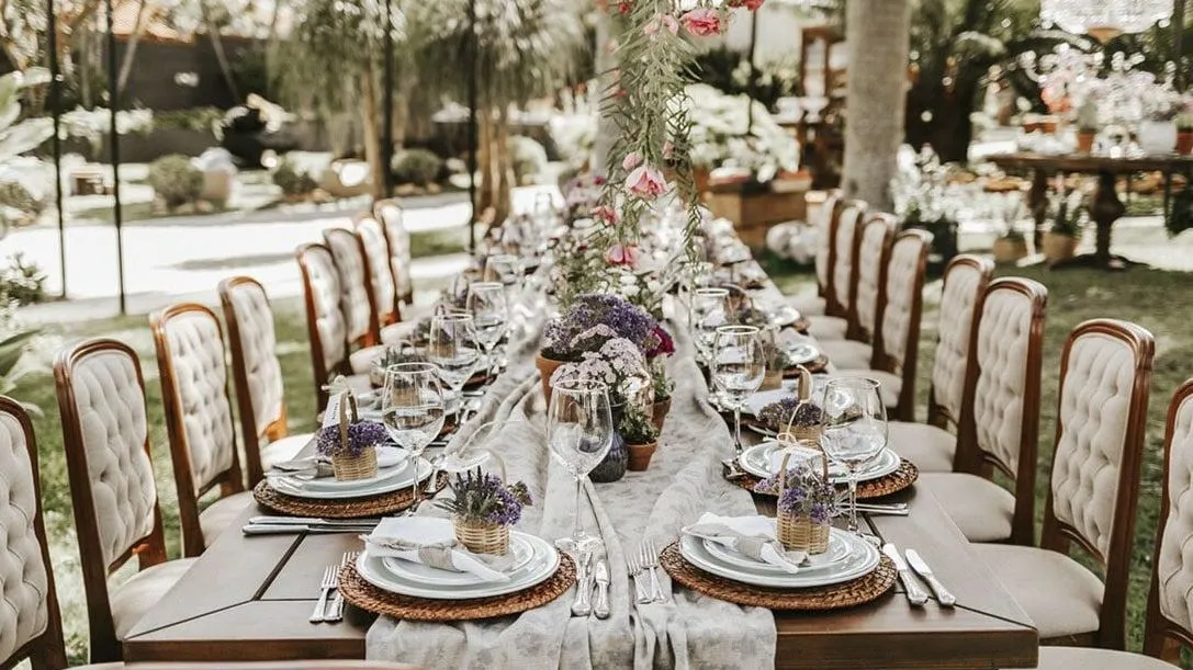 Uma longa mesa com pratos, copos e flores está posta para uma recepção de casamento.