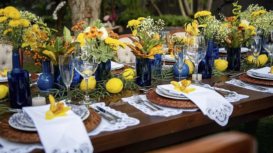 Uma mesa posta para um jantar com pratos, guardanapos, copos e vasos de flores.